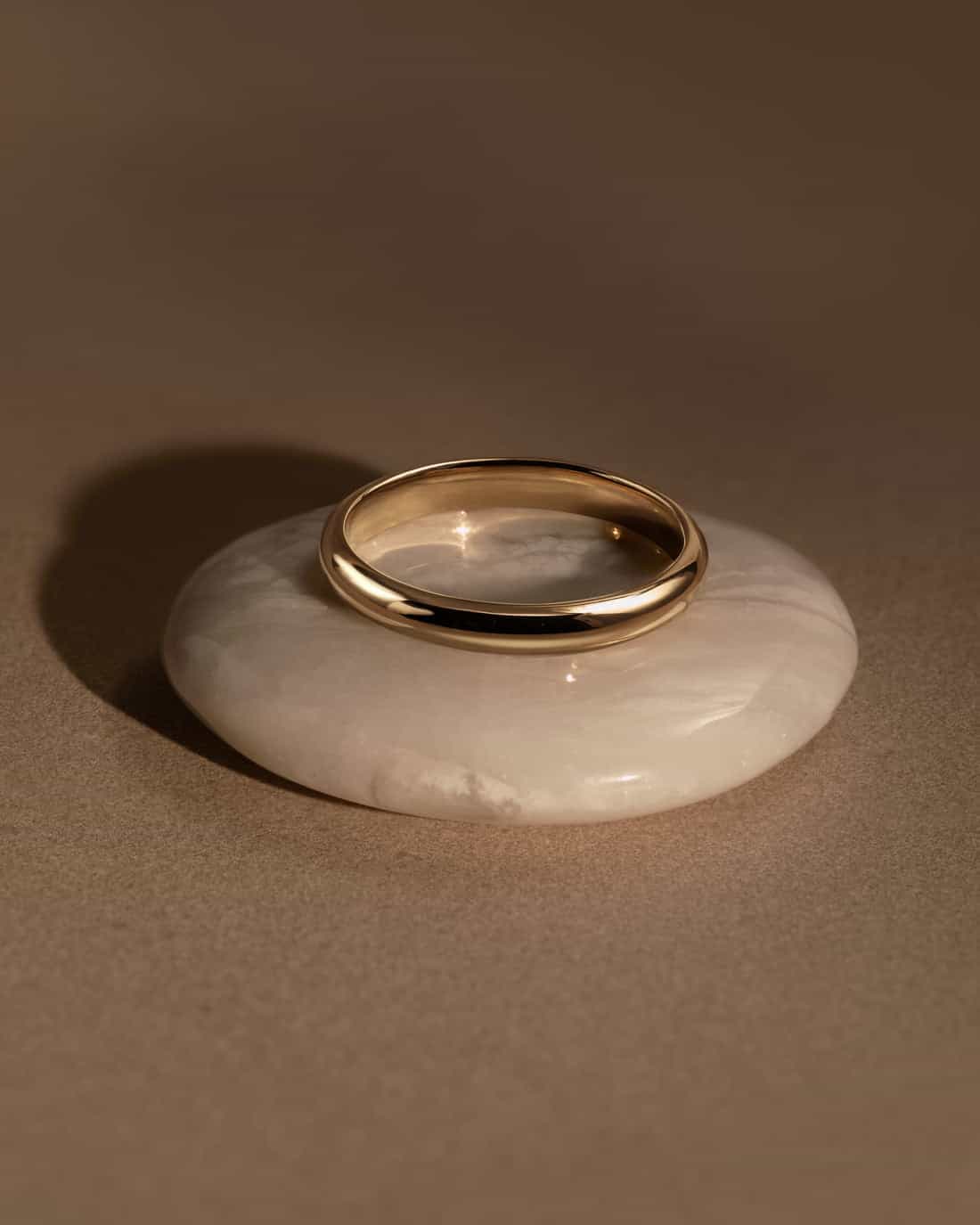 Anneau d'or 19kt poli, posé sur un galet de marbre blanc